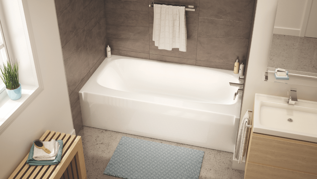 TO_3060_Soak_Deco2-EDIT CROP Bathroom with a white bathtub with taupe-brown tiling on the walls with a hanging white towel and light blue bath mat next to a light wooden bench and plant in the windowsill